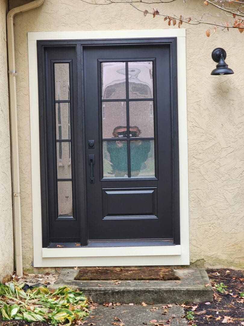 A black door with two windows and a brown mat.